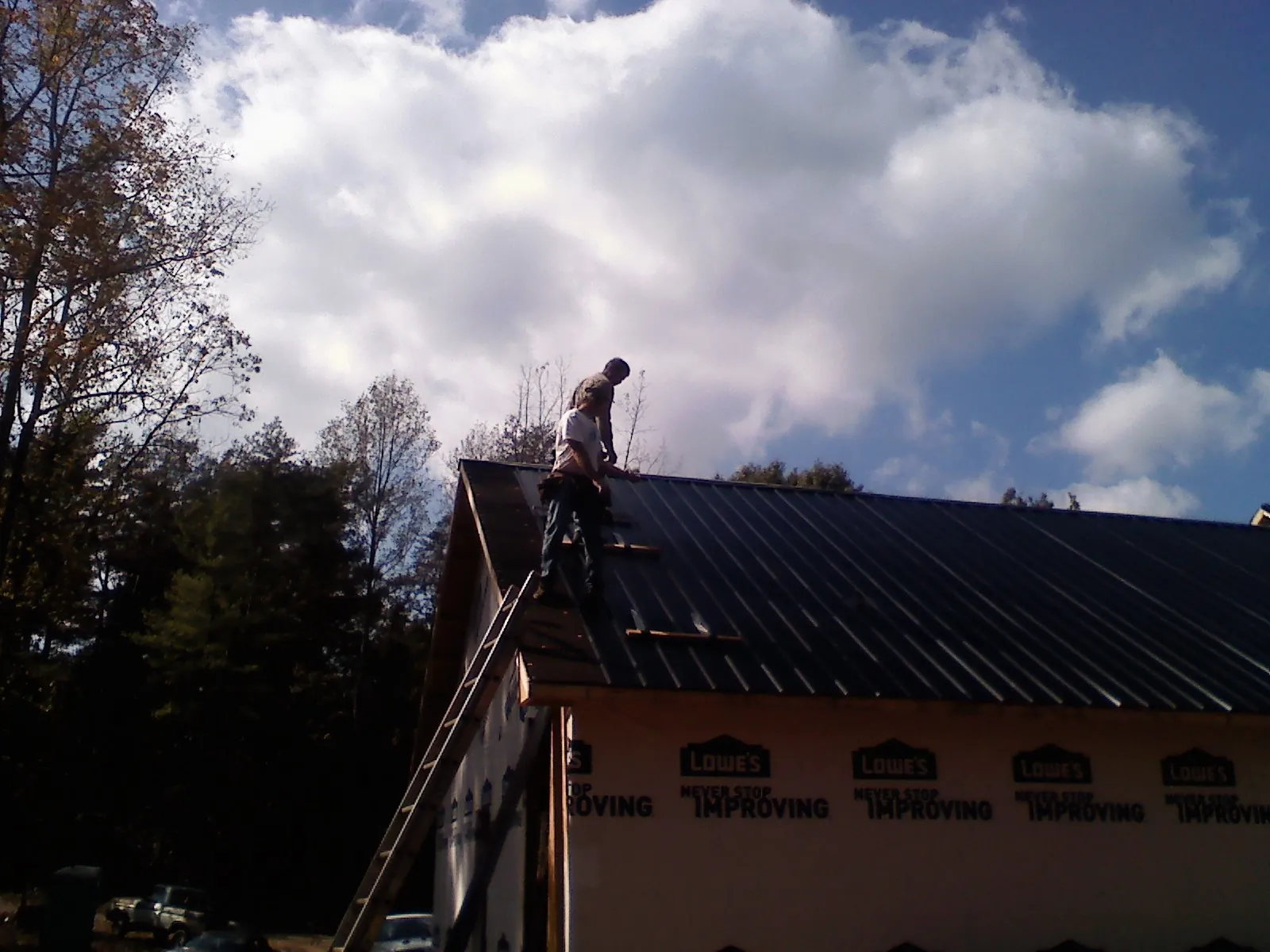 Roofer fastening dark metal panels high against a cloudy sky, from a Roof Inspection job in Klickitat