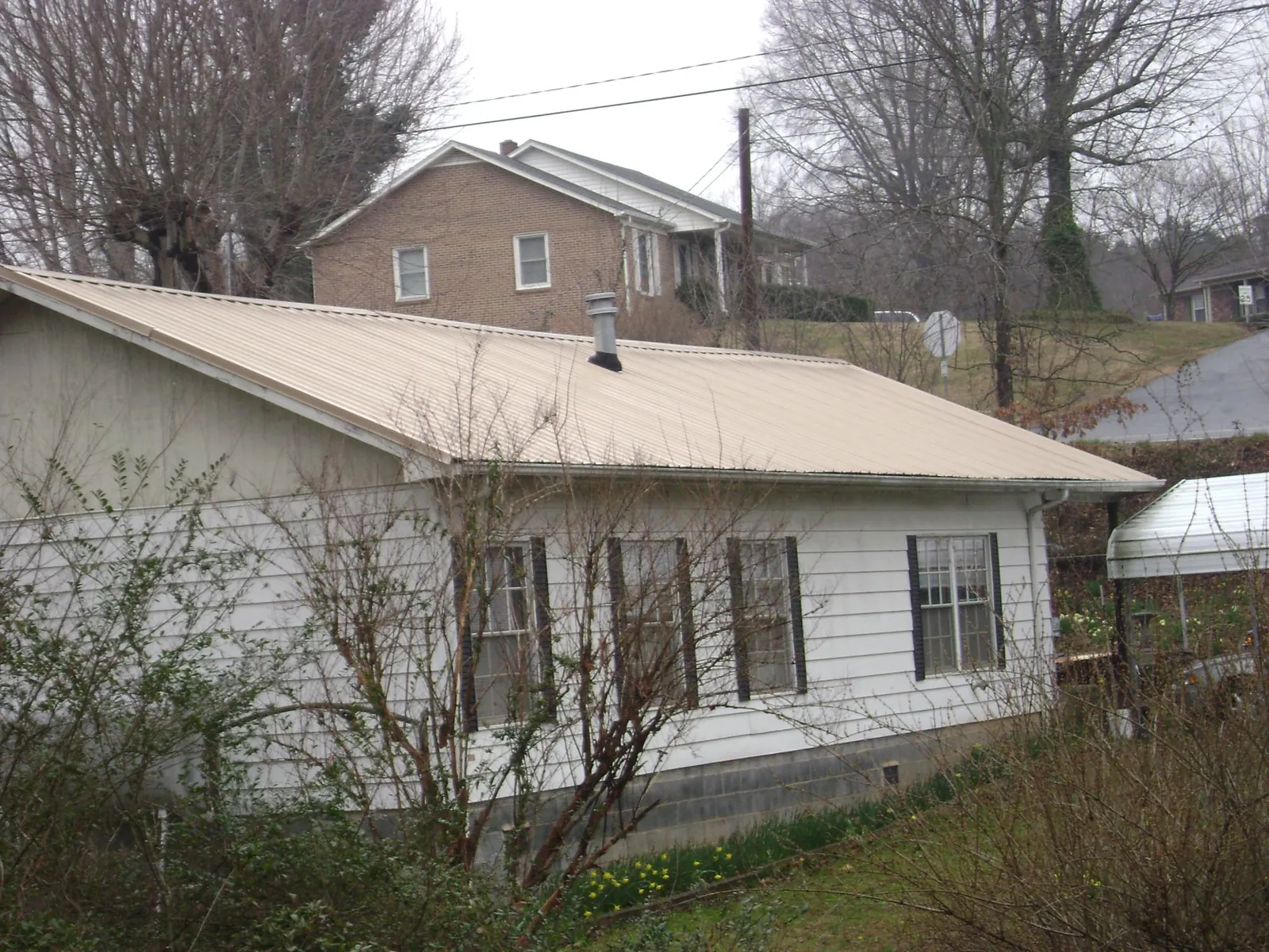 Tan metal roof on a white sided house set into a hillside — Commercial Roofing by Roofing Brothers in Klickitat